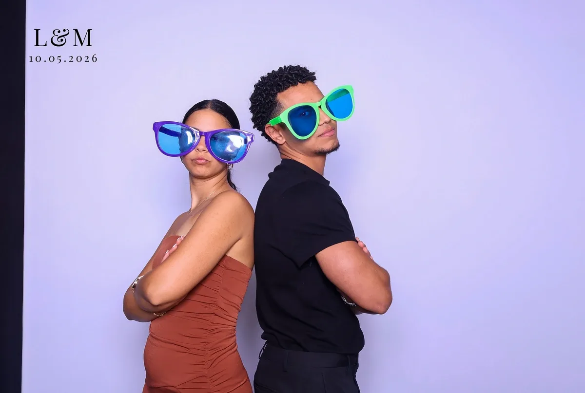 Two guests in oversized novelty glasses striking a back-to-back pose on a Magic Mirror print at an engagement party