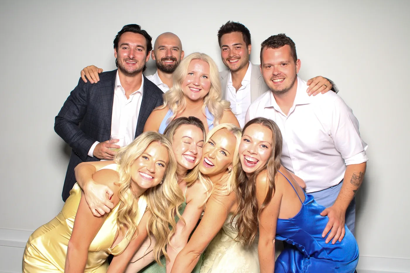 Nine wedding guests in satin dresses and open collars squeezed into one laughing frame at the Pic Booth photo booth