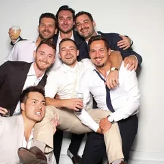 Groomsmen piled together with drinks raised